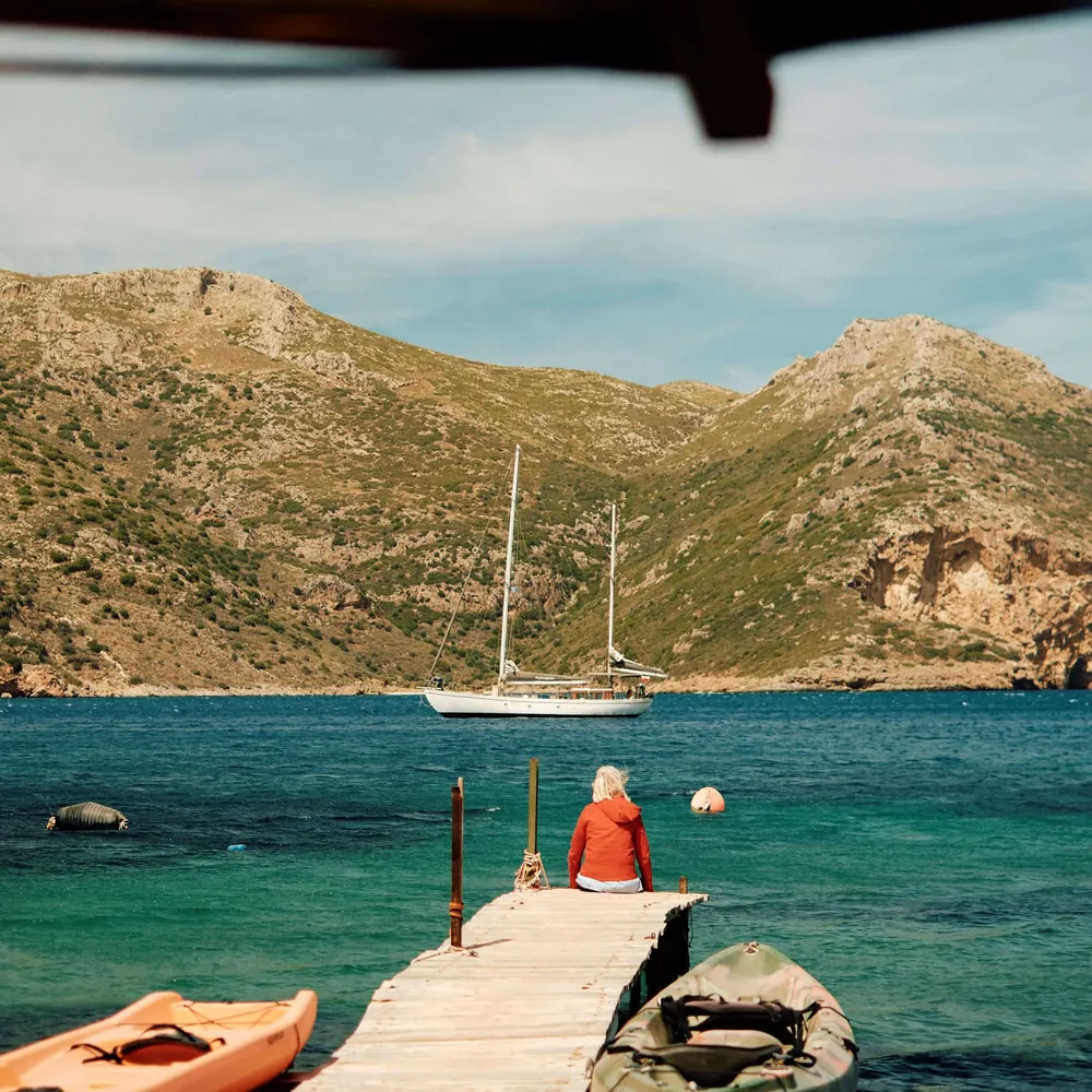 A solo traveller on the pier, overlooking the sea and boats, in the Mani, Greece's Peloponnese