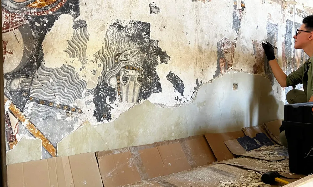A volunteer removing lime wash to reveal an intricate wall painting on a church in Transylvania