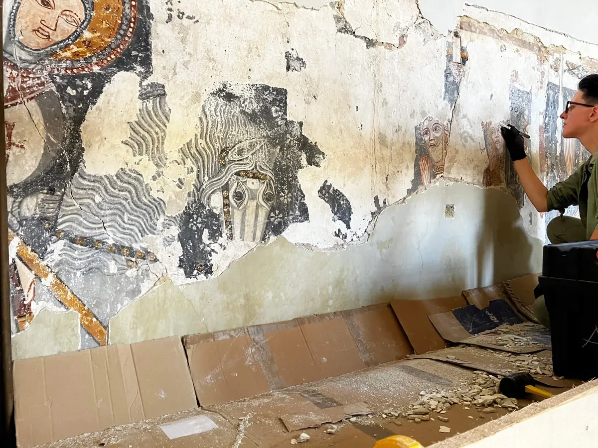 A volunteer removing lime wash to reveal an intricate wall painting on a church in Transylvania