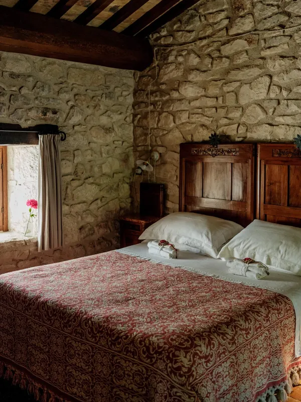 A bedroom in Case Catalona, with stone calls and a traditional red bed spread