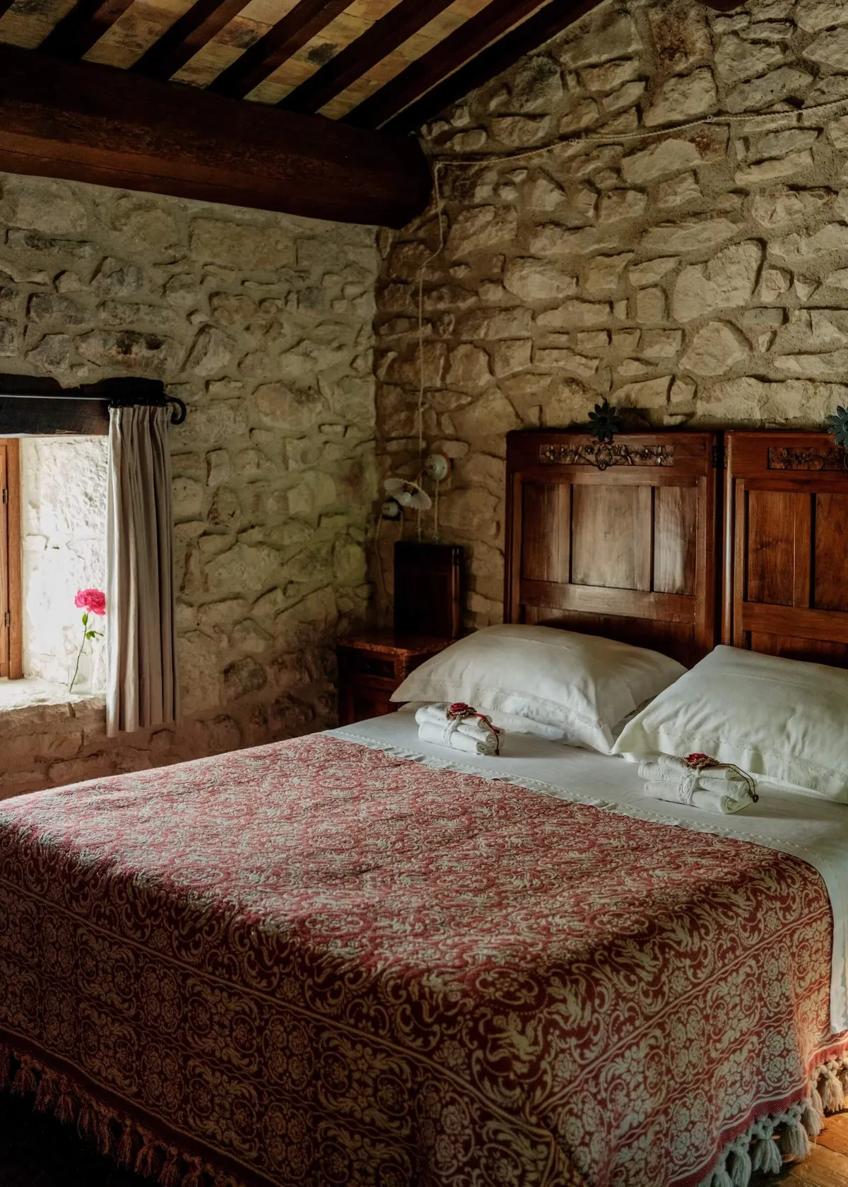A bedroom in Case Catalona, with stone calls and a traditional red bed spread