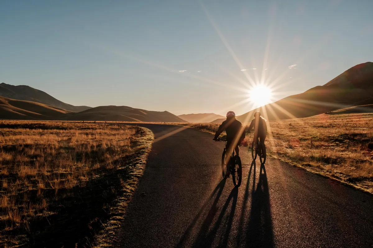 Cyclists on road at sunset with hills in background, Campo Imperatore, Abruzzo, Italy
