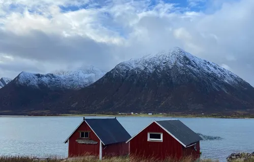 Traditional red timber houses by coast against snowy mountain backdrop Vesteralen, Norway