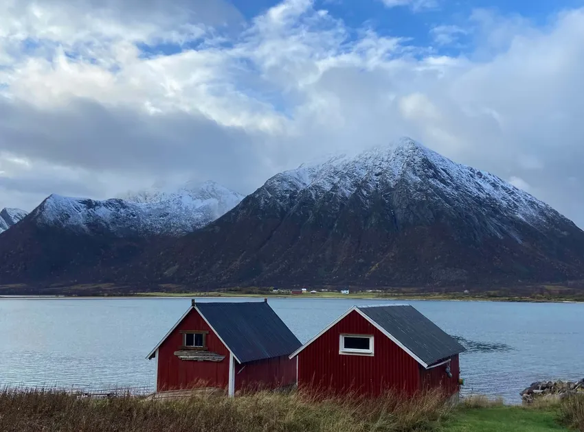 Traditional red timber houses by coast against snowy mountain backdrop Vesteralen, Norway