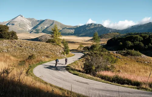 Two cyclists going uphill on road, mountain background, Campo Imperatore, Abruzzo, Italy
