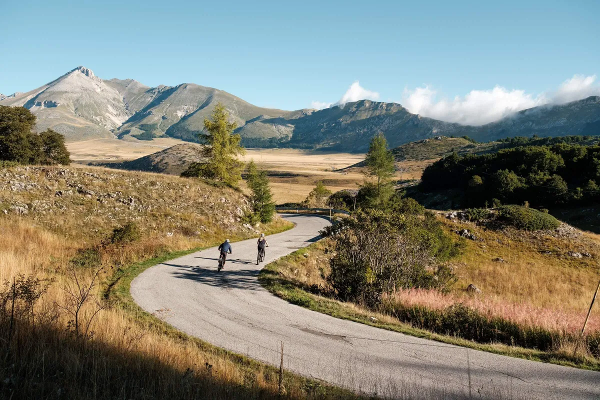 Two cyclists going uphill on road, mountain background, Campo Imperatore, Abruzzo, Italy