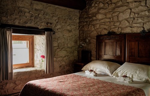 Wid shot of wooden bed with red blankets in stone walled bedroom with rustic window, Case Catelano, Abruzzo, Italy